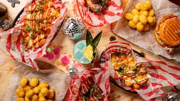 On propose une variété de plats, notamment des pommes de terre en forme de petits cubes, des ailes de poulet et un hamburger, le tout servi sur des plateaux recouverts de papier.