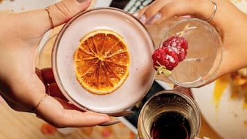 Dos manos sosteniendo un vaso con una rodaja de naranja y una frambuesa.