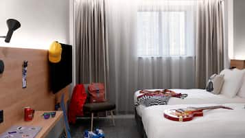 A hotel room with a bed, a desk, a chair, a TV, a window with curtains, and a guitar.