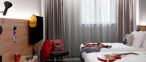 A hotel room with a bed, a desk, a chair, a TV, a window with curtains, and a guitar.