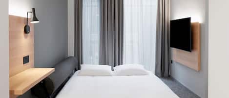 A modern hotel room with a bed, a wooden shelf, a wall-mounted TV, and a window with curtains.