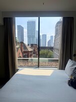 Habitación de hotel con una cama grande, vistas a la ciudad a través de ventanales del suelo al techo y un diseño de interiores moderno.