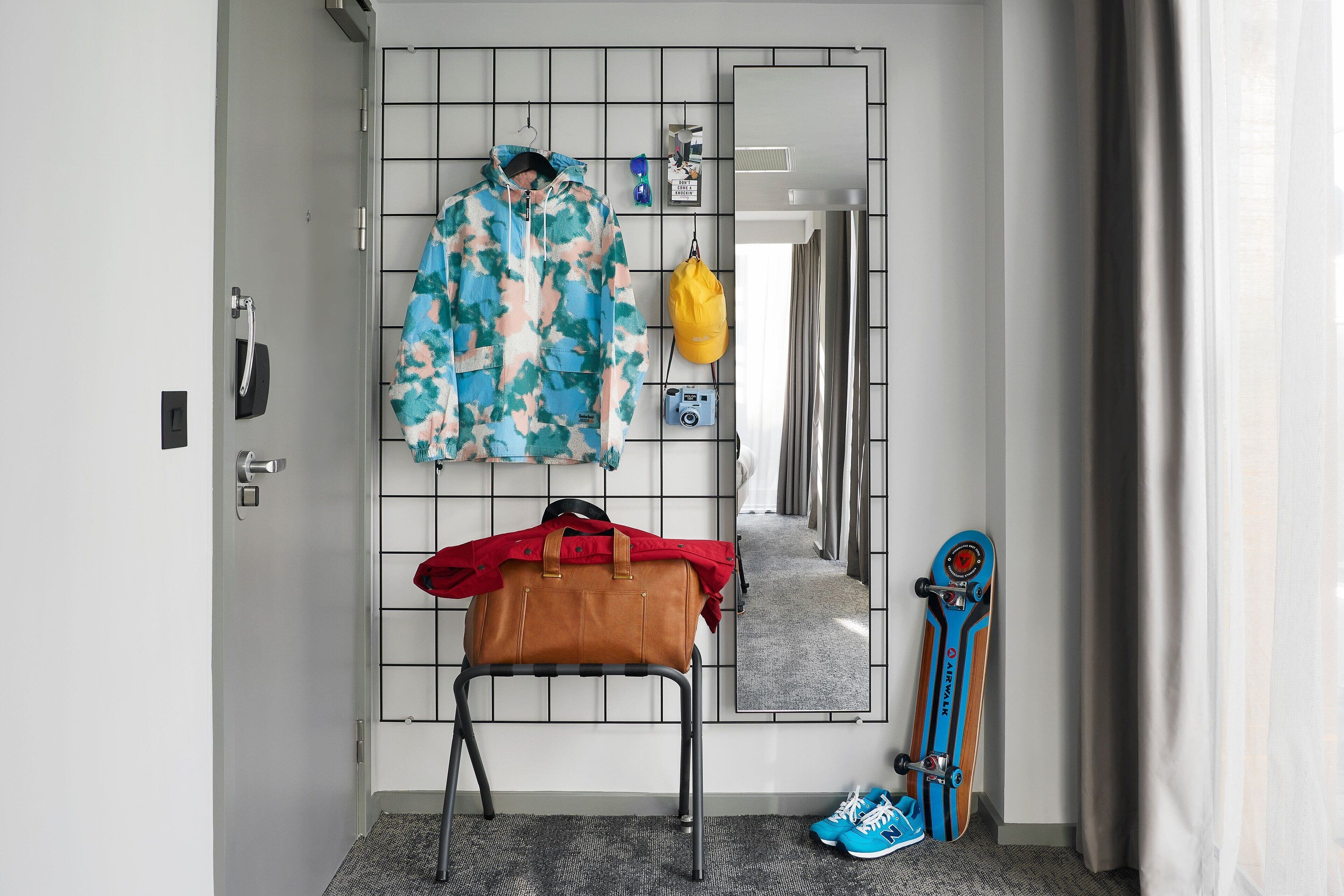 Un couloir avec une porte, un porte-manteau avec une veste, un sac rouge, un appareil photo et une planche de skate bleue.