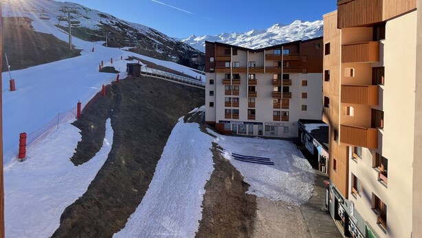 A modern building with multiple balconies, a ski slope in the background, and a clear sky.