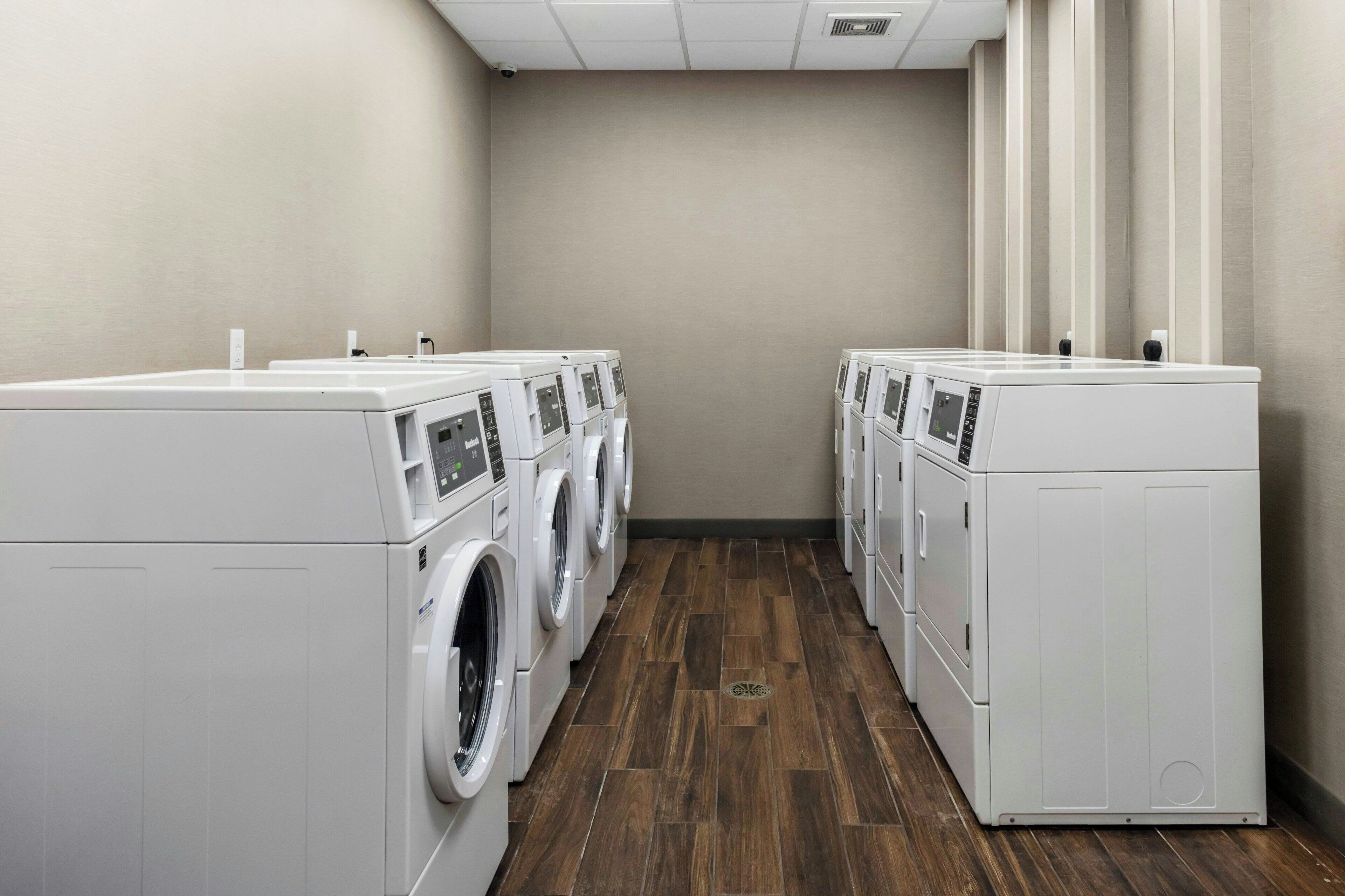 A laundry room with four white front-loading washers and dryers arranged in a row.
