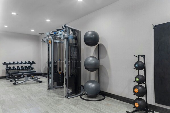 A gym with a weight bench, dumbbells, a squat rack, and exercise balls.