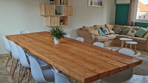 Un salon avec une table à manger en bois, des chaises blanches, un canapé d’angle beige et une plante en pot.