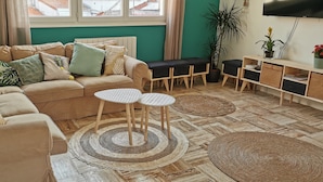 Un salon avec un canapé beige, deux tables rondes, une table basse en bois et un téléviseur fixé au mur.