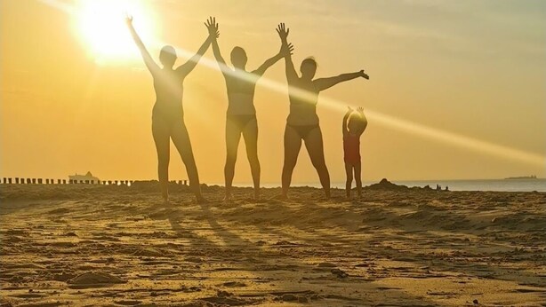 Une scène de plage au coucher du soleil, avec des silhouettes de personnes et deux verres de bière posés sur le sable.