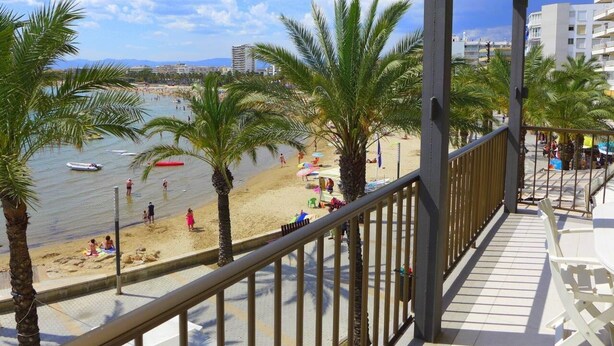 Een balkon met uitzicht op een strand, palmbomen en een heldere lucht.