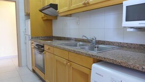Een keuken met houten kastjes, een granieten aanrecht, een roestvrijstalen spoelbak, een magnetron, een vaatwasser en een inbouwoven.