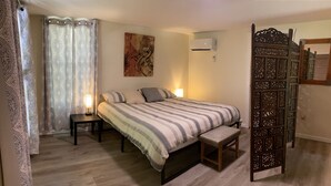 Ein Schlafzimmer mit einem Bett, Nachttischen, einer Bank, einer Wand-Klimaanlage und einem dekorativen Raumteiler.