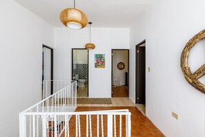 A hallway with white walls, a white railing, and a woven ceiling light fixture.