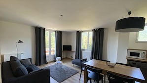 A modern living room with a sofa, a dining table, chairs, a TV, and a kitchen area with a microwave. - 6/8 pers apartment in the heart of the Chartreuse at the foot of the ski slopes (Sarcenas)