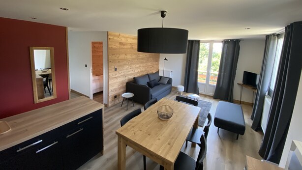 A modern living space with a wooden dining table, black sofa, and a large black pendant light. - 6/8 pers apartment in the heart of the Chartreuse at the foot of the ski slopes (Sarcenas)