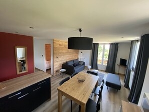 A modern living space with a wooden dining table, black sofa, and a large black pendant light.