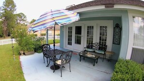 Un patio couvert avec une table et des chaises, un parasol à rayures et un petit banc.