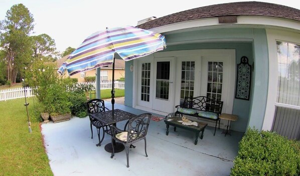A covered patio area with a table and chairs, a striped umbrella, and a small bench. - PrimoFish Golf Villa (Gautier)