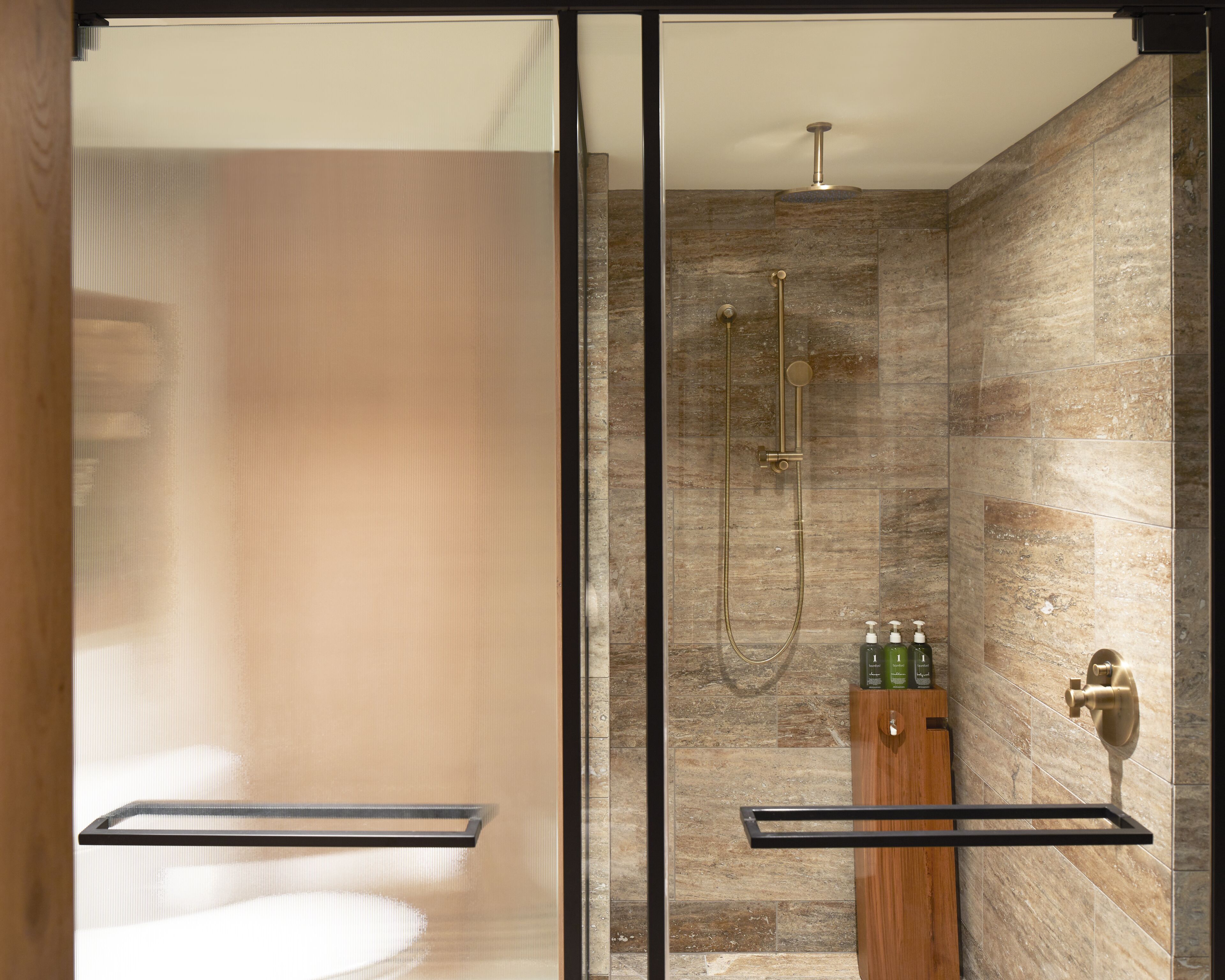 A modern bathroom with a glass shower enclosure, a wooden vanity with toiletries, and a marble-tiled shower wall.