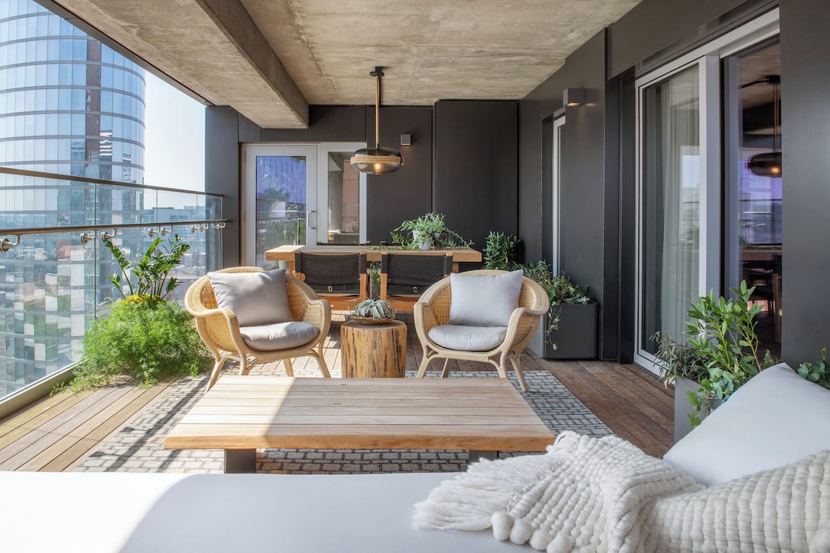 Ein Balkon mit Korbstühlen, einem Holztisch und Topfpflanzen.