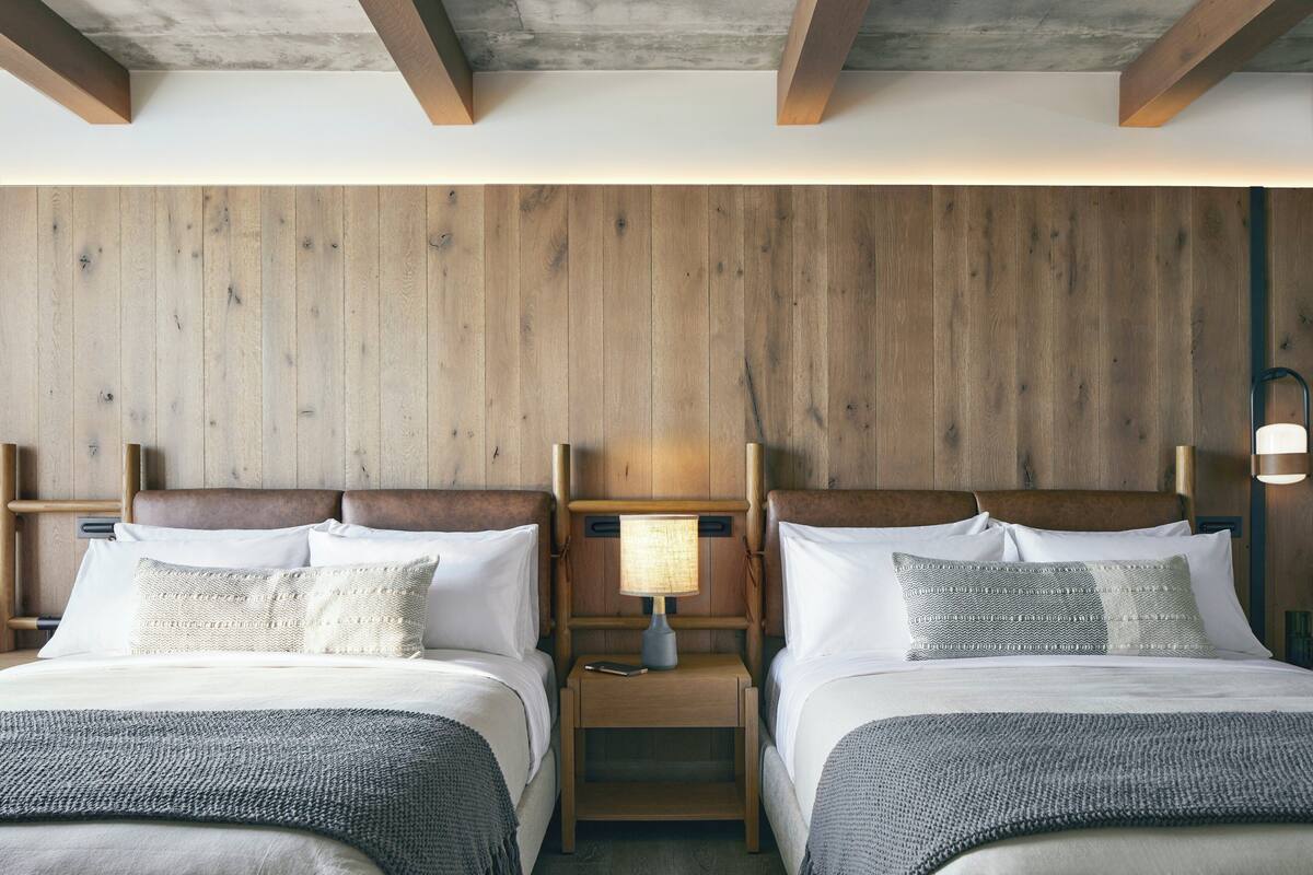 Ein Doppelbett mit Holz-Kopfteil, ein Nachttisch mit Lampe sowie ein weiterer Nachttisch mit Telefon.