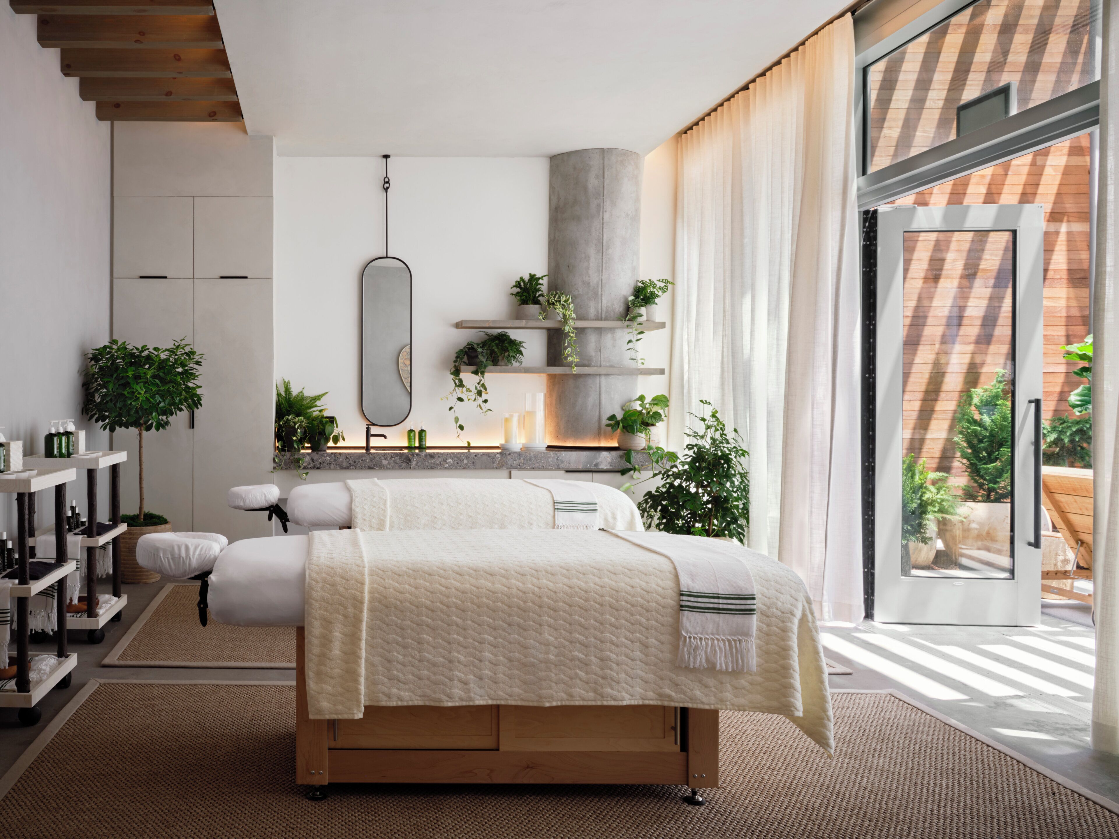 Un dormitorio moderno con cama, mesitas de noche, un espejo y vistas al exterior.