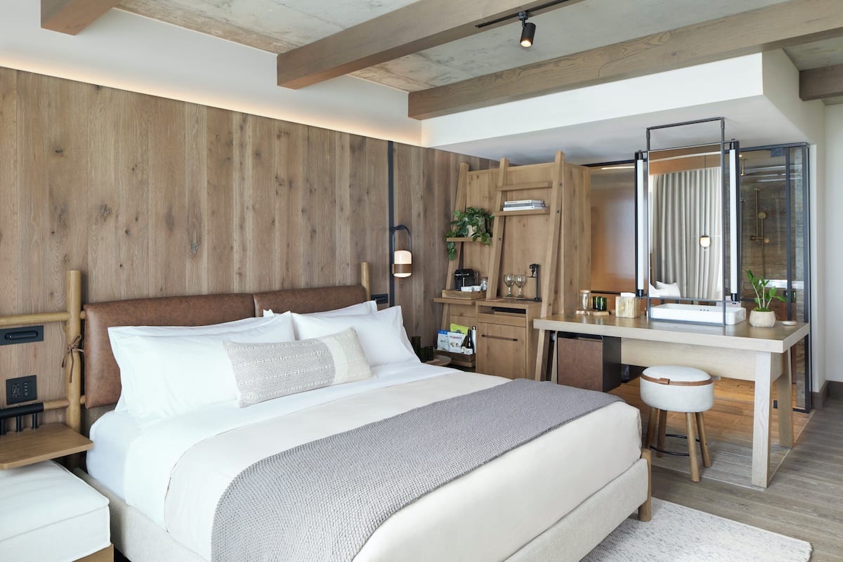 Ein modernes Schlafzimmer mit einem hölzernen Kopfteil, einem großen Bett, einem Schreibtisch mit Spiegel und einer Duschkabine.