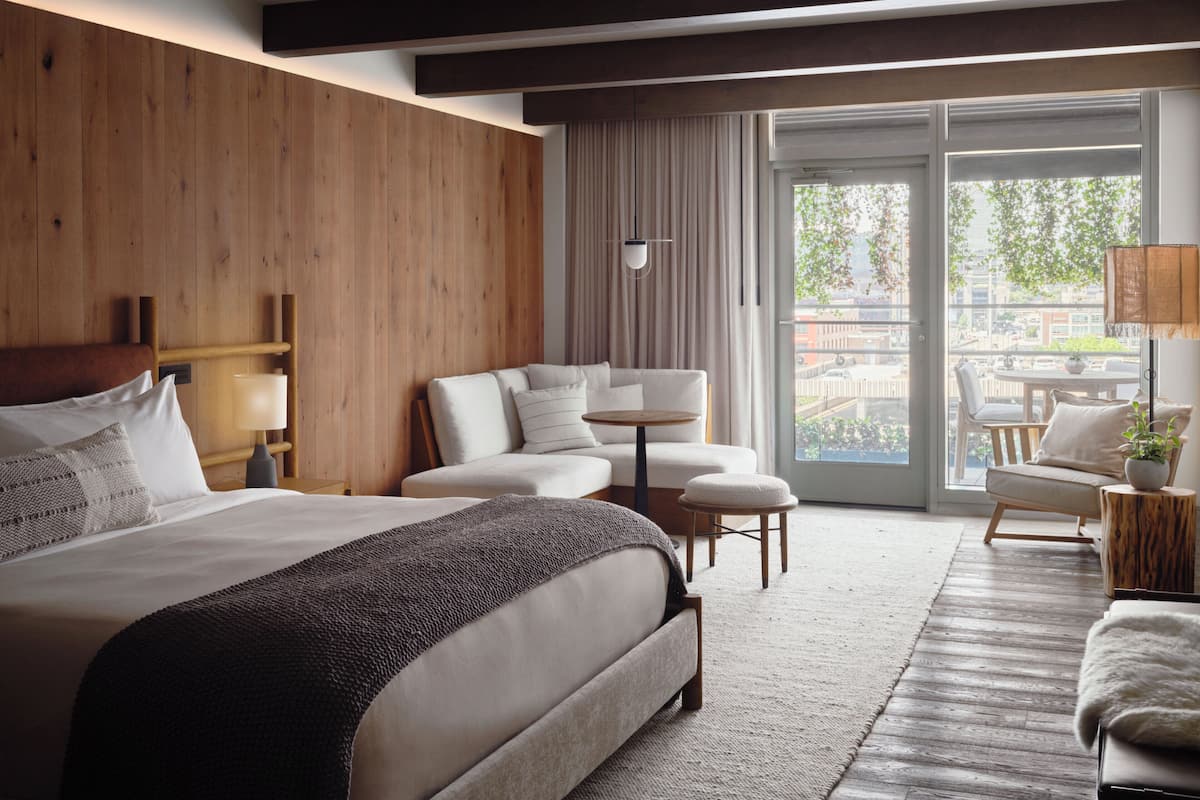 Ein modernes Hotelzimmer mit einem großen Bett, einer Sitzecke, einem kleinen Tisch und Blick ins Freie.