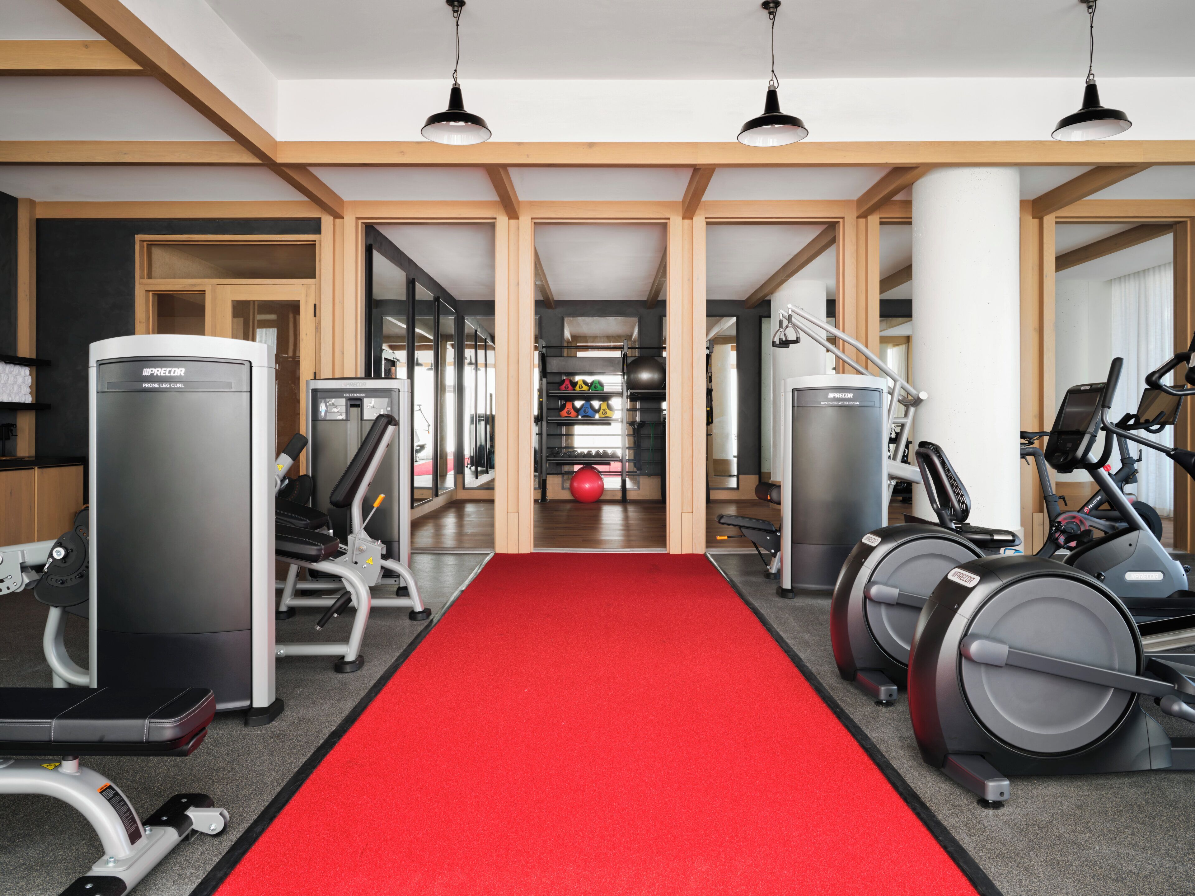 A gym with exercise equipment, a red carpet, and wooden beams on the ceiling.