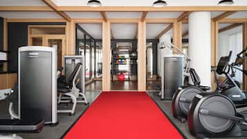 Un gimnasio con equipamiento de ejercicio, alfombra roja y vigas de madera en el techo.