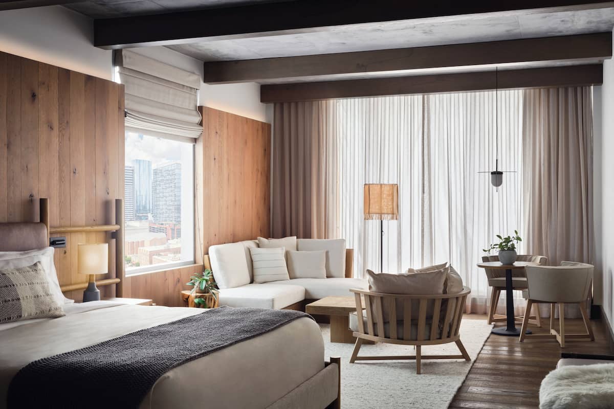 Ein modernes Hotelzimmer mit einem großen Bett, einer Couch, einem Sessel, einem kleinen Tisch und Blick auf die Stadt.