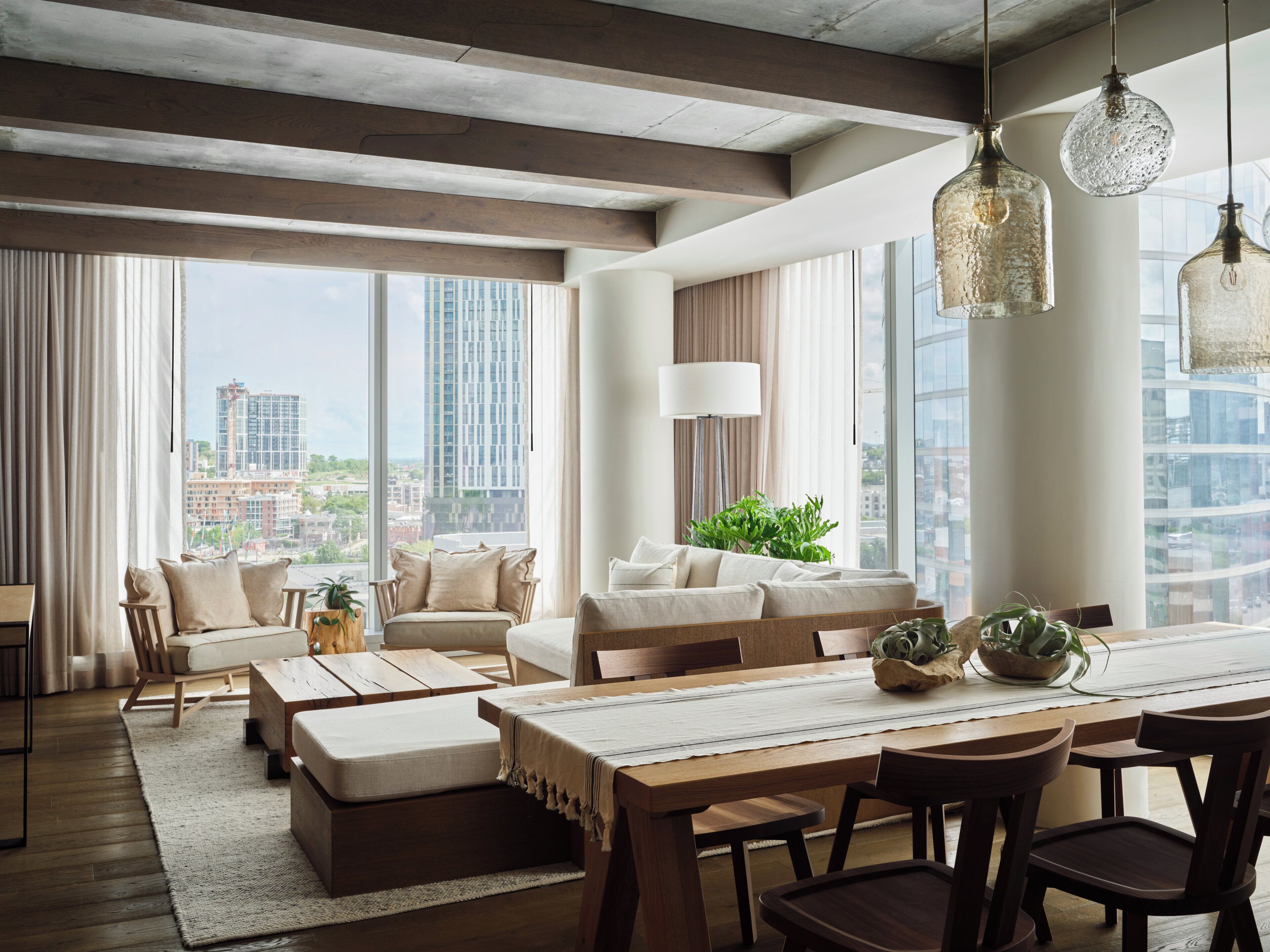 A modern living room with a large window, a sofa, a dining table, and hanging light fixtures.