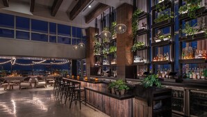 A bar area with wooden bar counters, seating, and shelves with bottles. - 1 Hotel Nashville (Nashville)