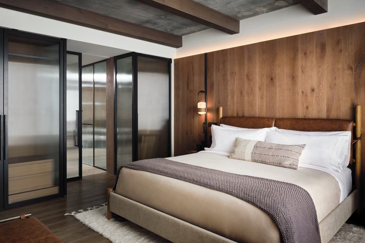 Ein Schlafzimmer mit einem großen Bett, Holzwandverkleidung, einer Glastür zu einem anderen Raum und einem Nachttisch mit Lampe.