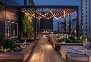 Une terrasse sur le toit avec une plateforme en bois, des espaces de détente, une petite fontaine et des guirlandes lumineuses.