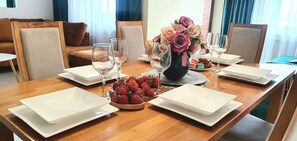 Une table à manger dressée avec de l’assiette blanche, des verres, un vase de fleurs et un saladier de fraises.