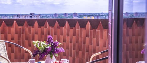 A balcony with wicker chairs, a table with a vase of purple flowers, a bowl of strawberries, and a cup.