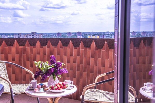 A balcony with wicker chairs, a table with a vase of purple flowers, a bowl of strawberries, and a cup.