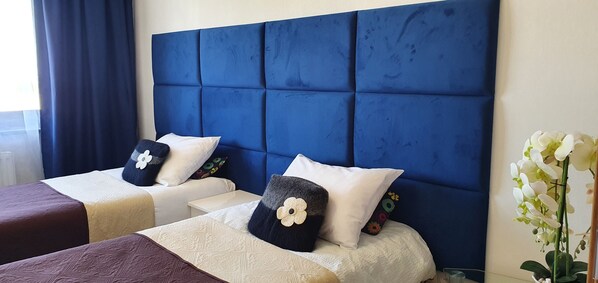 A hotel room with two beds, each with a headboard and pillows, a small table, and a vase with flowers.