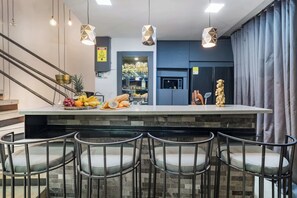A modern kitchen with a central island, bar stools, and hanging pendant lights.