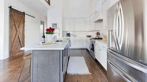 A spacious kitchen with a large island, stainless steel appliances, and a rustic wooden door.