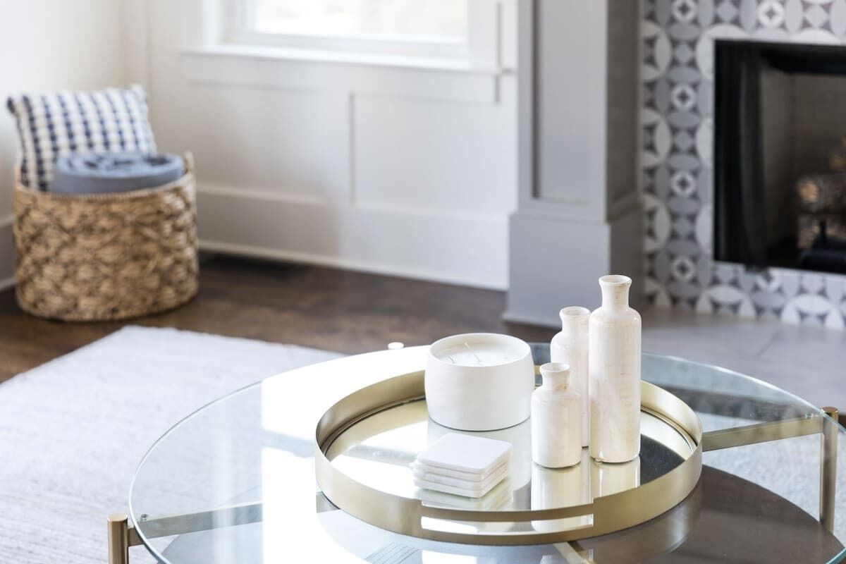 A round glass table with a gold frame, holding a white candle, a small white container, and two white bottles.