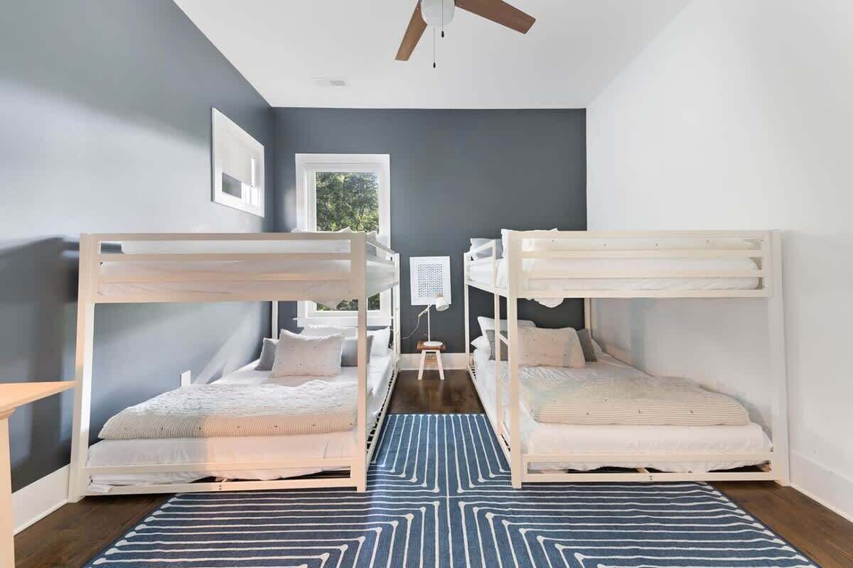 Une chambre avec deux lits superposés, un ventilateur de plafond, une fenêtre et un tapis à motifs.