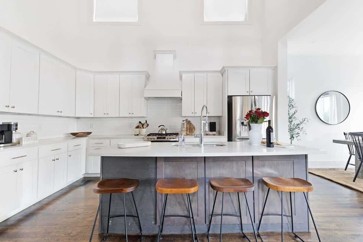 A modern kitchen with white cabinetry, a central island with stools, and a stainless steel refrigerator.