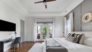 A modern bedroom with a large bed, a desk, and a ceiling fan.