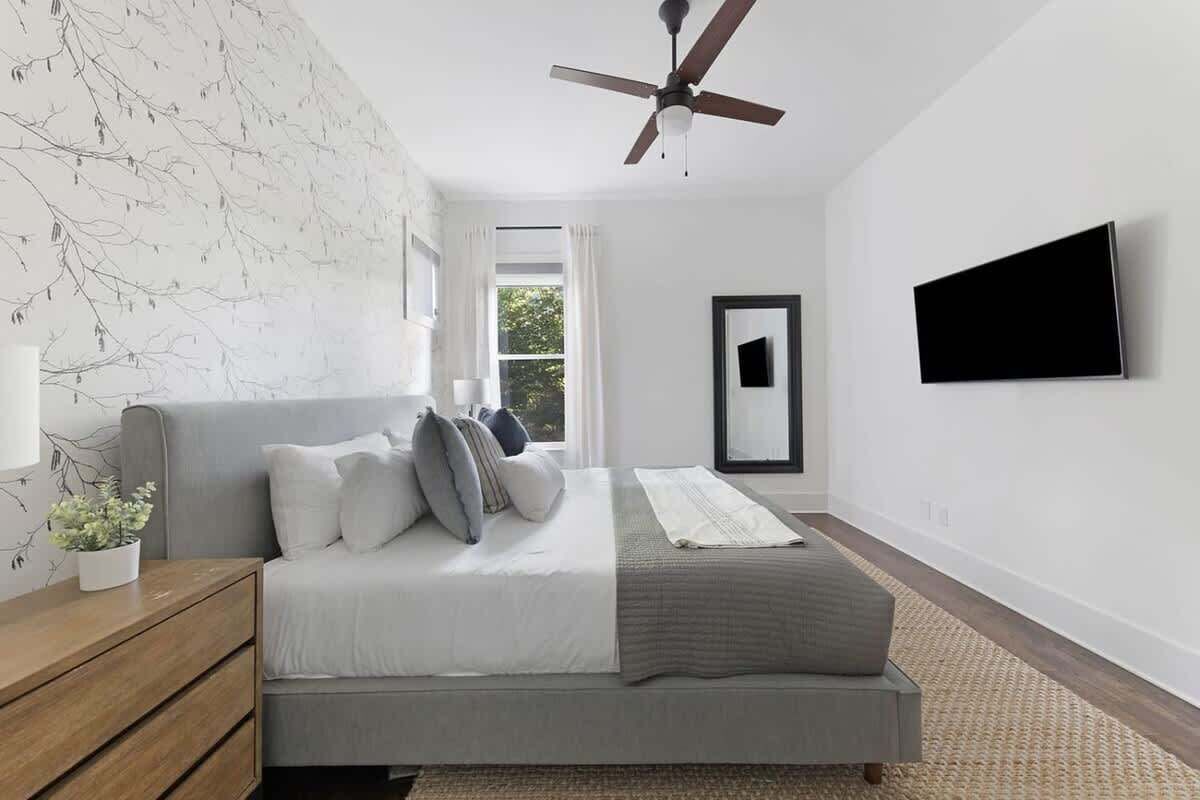 A bedroom with a bed, a ceiling fan, a TV, and a window with curtains.