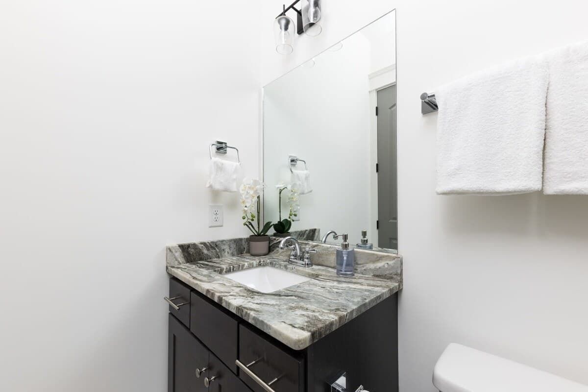 A modern bathroom with a marble sink, dark cabinets, a large mirror, and white towels.