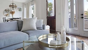 A modern living room with a grey sofa, a glass coffee table, and a dining area with a table and chairs.