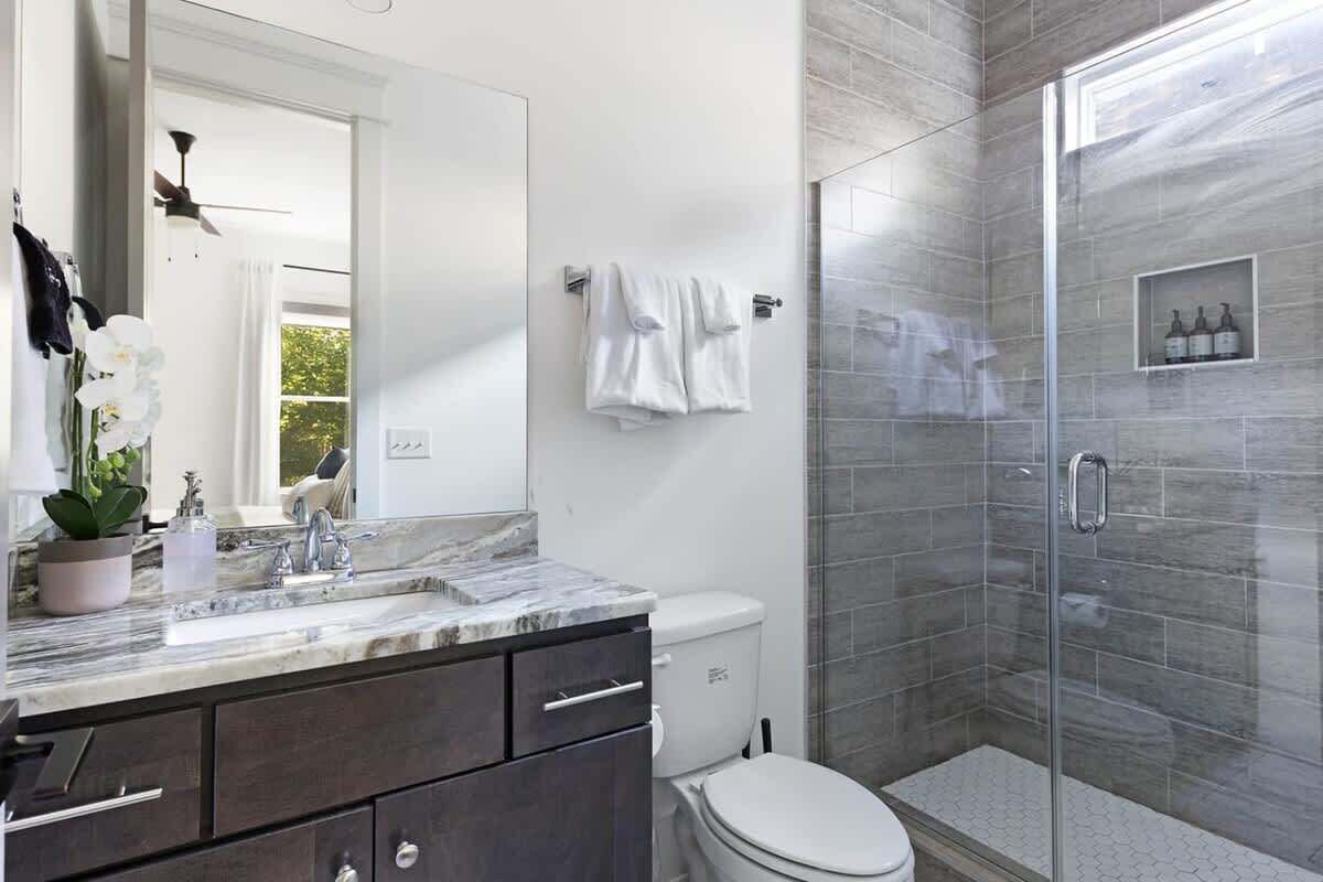 A modern bathroom with a marble sink, dark cabinets, a white toilet, and a glass-enclosed shower.