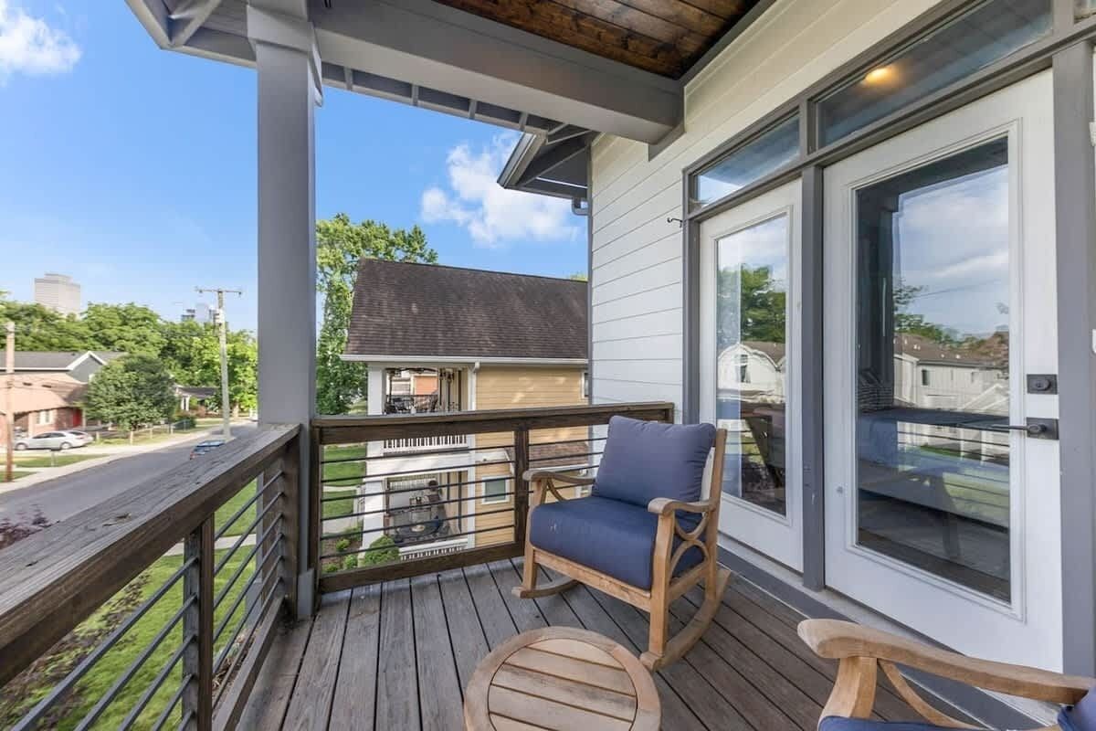 A wooden deck with a rocking chair and a small table, overlooking a residential street.